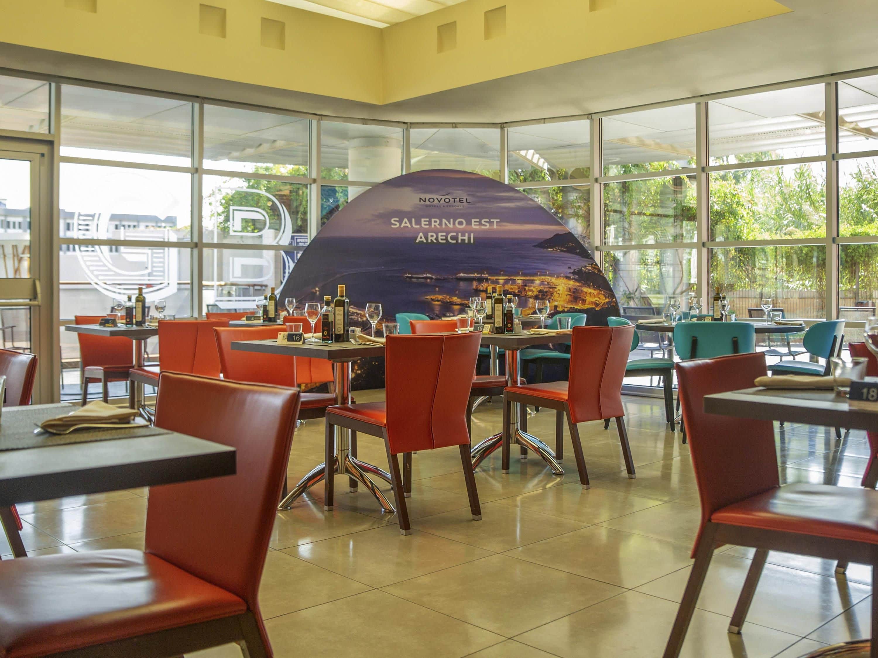 Un restaurante con mesas y sillas, un ventanal grande y un cartel con texto.
