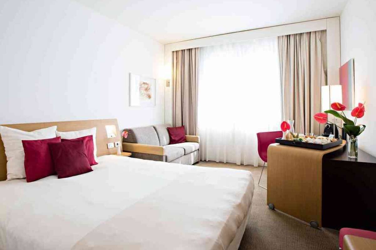 A hotel room with a large bed, a desk, a chair, and a sofa.