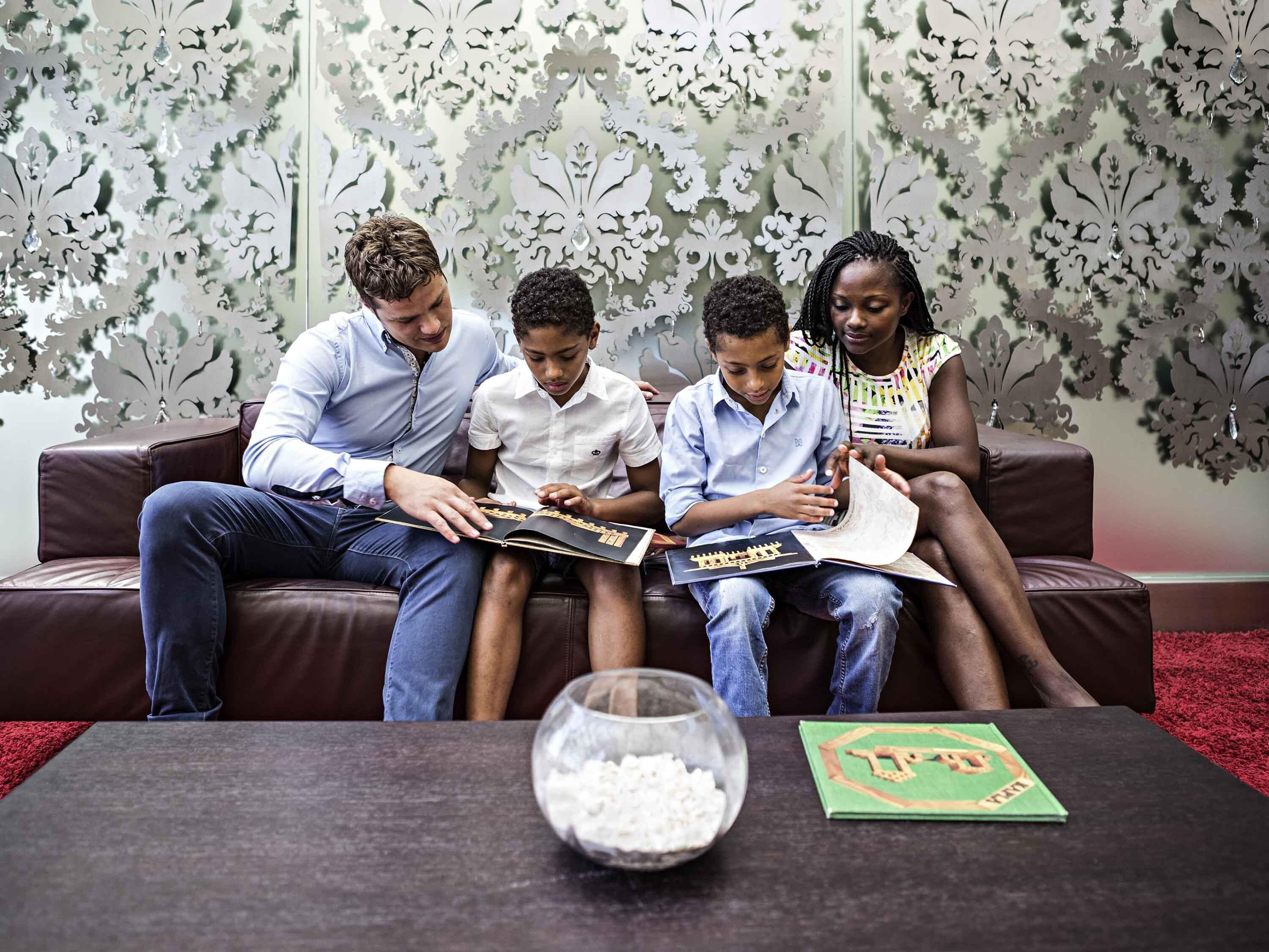 A group of four people sitting on a brown leather couch, reading a book together.