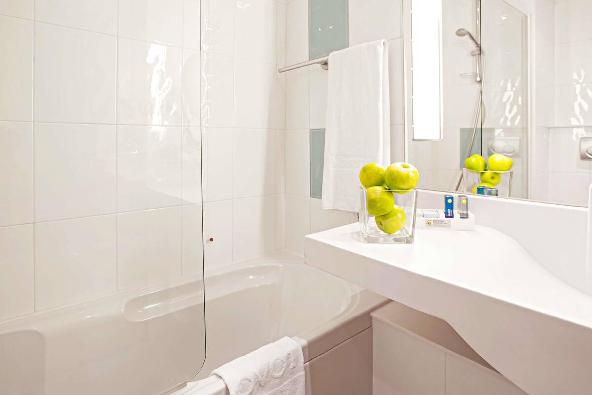 A modern bathroom with a white vanity, a glass vase with green apples, and a large mirror.