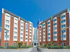 A modern hotel with a central entrance, multiple floors, and flags. - Hotel Novotel Salerno Est Arechi (Salerno)