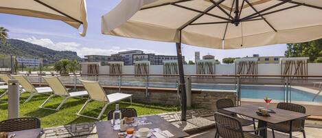 An outdoor patio area with tables and chairs, a swimming pool, and a view of buildings in the background.