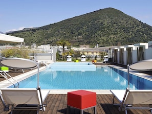 Una piscina al terrat amb vista a una muntanya, envoltada de gandules i una taula vermella.