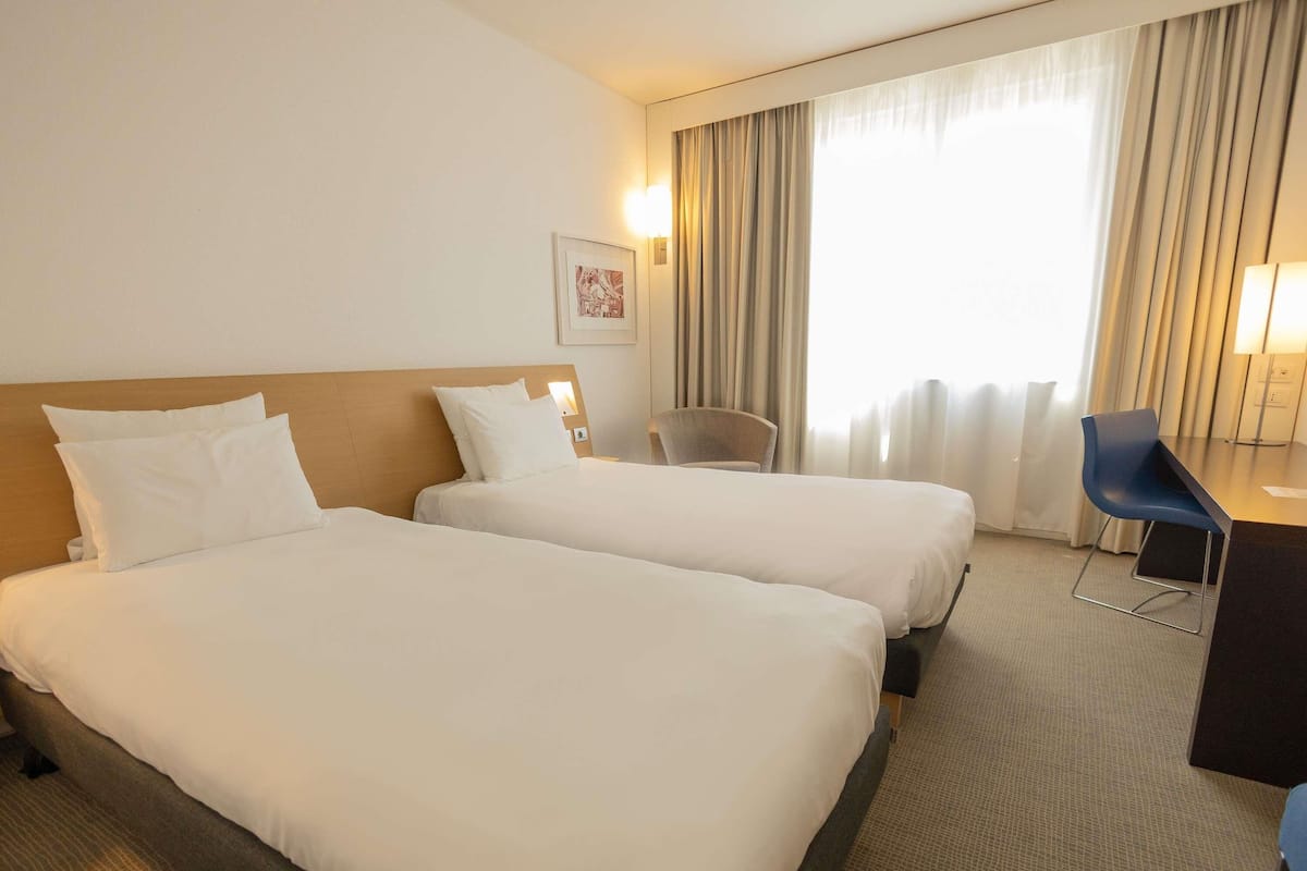 A hotel room with two beds, a desk, a chair, and a window with curtains.