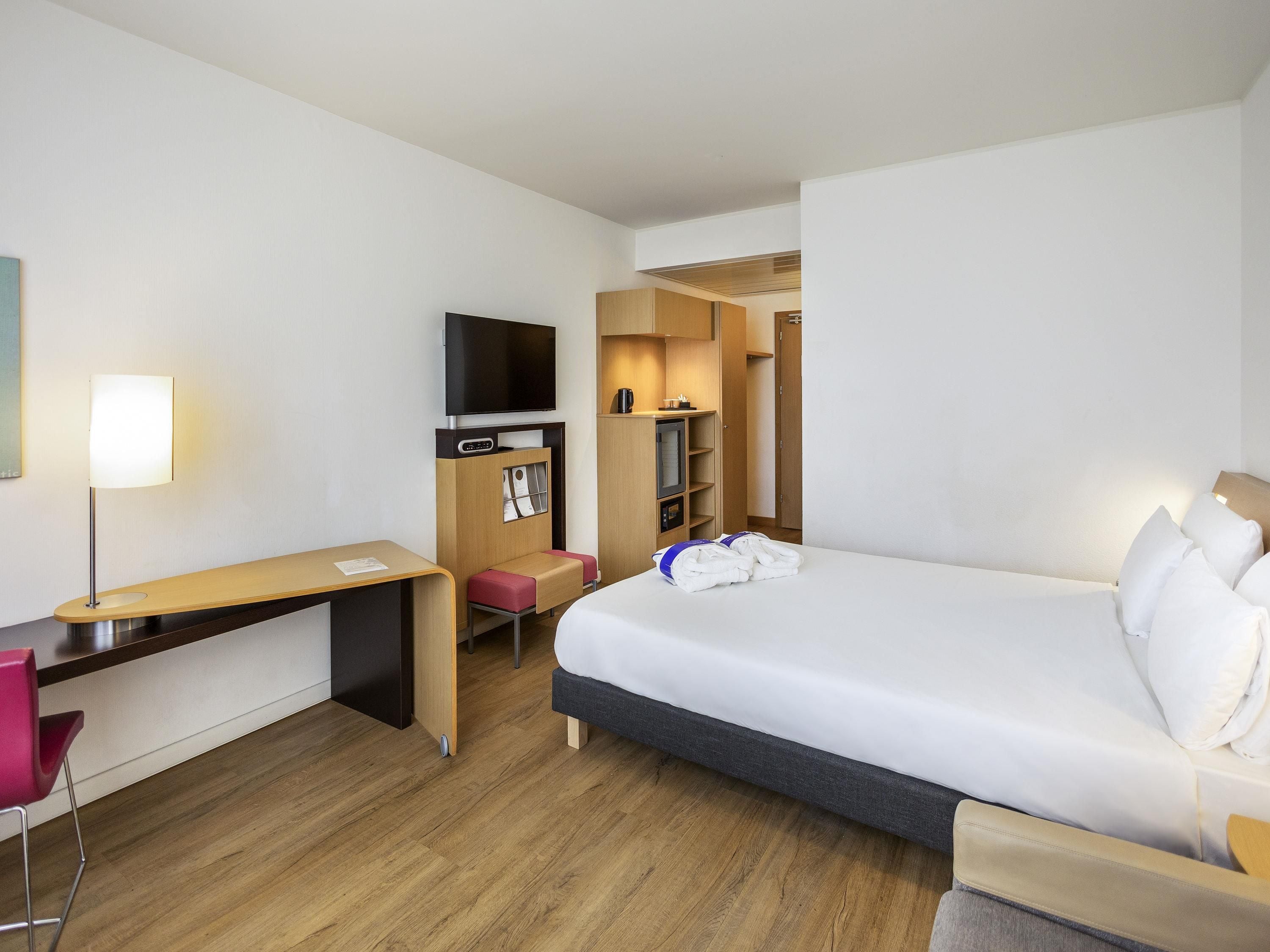 Una habitación de hotel con una cama, un escritorio, una silla, un televisor y un armario.