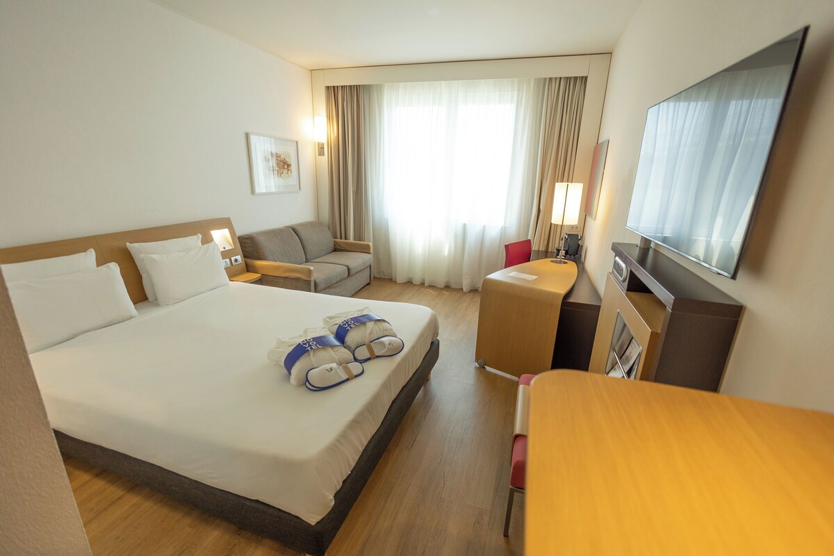 Una habitación de hotel con una cama grande, un sofá, un escritorio y una televisión.