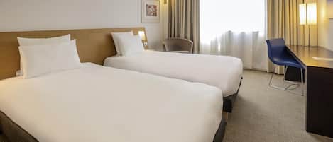 A hotel room with two beds, a desk, a chair, and a large window with curtains.