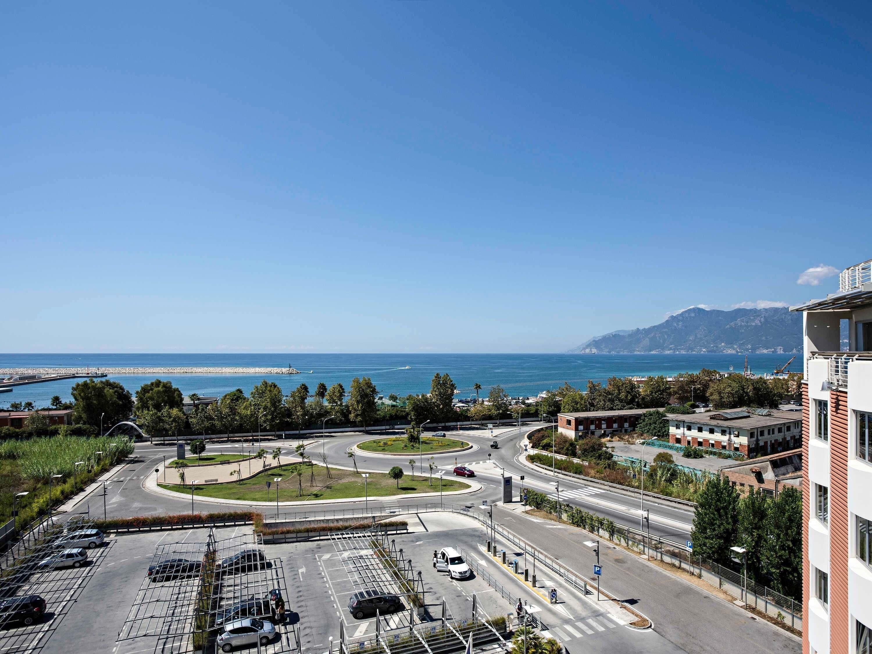 Un parking à plusieurs niveaux, doté de voies de circulation bien définies et offrant une vue sur la mer et les montagnes en arrière-plan.