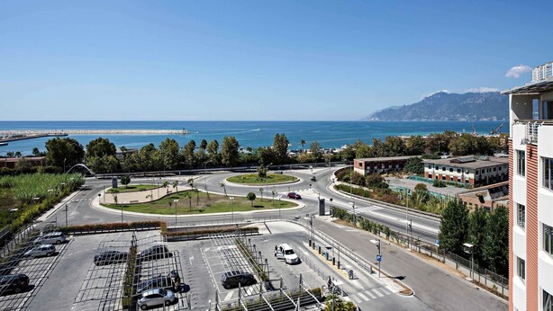 A multi-level parking structure with clear roadways and a view of the sea and mountains in the background. - Hotel Novotel Salerno Est Arechi (Salerno)