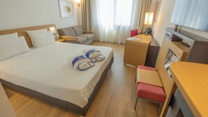 Una habitación de hotel con una cama grande, un escritorio, una silla, un sofá y un televisor.
