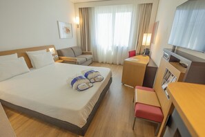 A hotel room with a large bed, a desk, a chair, a sofa, and a TV. - Hotel Novotel Salerno Est Arechi (Salerno)
