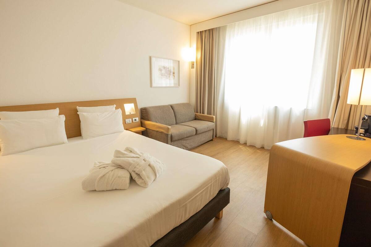 A hotel room with a large bed, a sofa, a desk, and a chair.