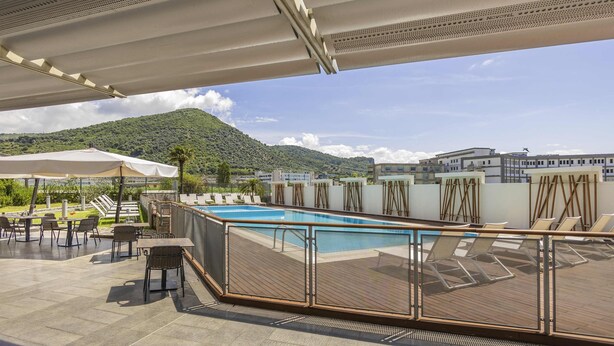 A rooftop pool area with lounge chairs and tables, a pool, and a view of a mountain. - Hotel Novotel Salerno Est Arechi (Salerno)