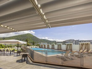 A rooftop pool area with lounge chairs and tables, a pool, and a view of a mountain. - Hotel Novotel Salerno Est Arechi (Salerno)