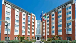 A modern hotel with a central entrance, multiple floors, and flags. - Hotel Novotel Salerno Est Arechi (Salerno)