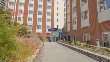 Un hôtel au design moderne, doté d’une entrée centrale, d’une allée couverte et d’un jardin aménagé avec des fleurs.