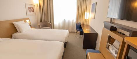 A hotel room with two beds, a desk, a chair, a television, and a window with curtains.
