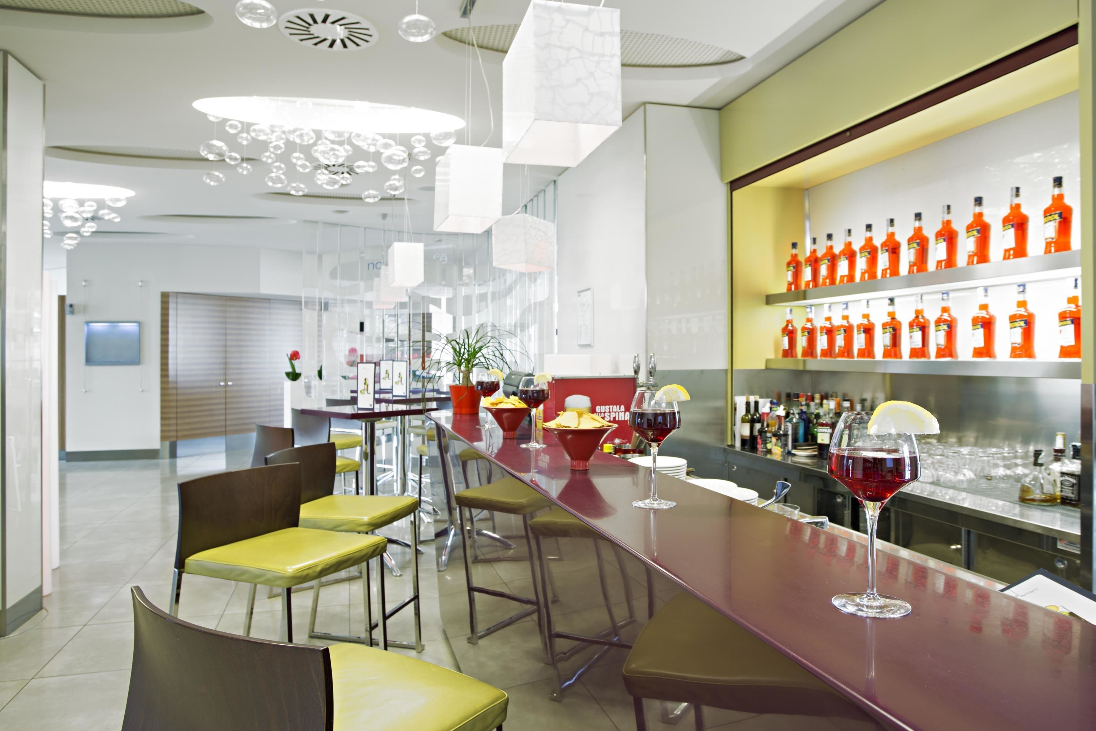 Un bar moderno con una barra alargada, varios taburetes y una gran variedad de botellas en estanterías.