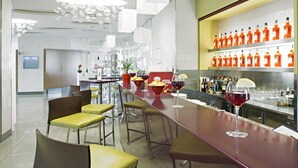 A modern bar area with a long counter, multiple stools, and a variety of bottles on shelves. - Hotel Novotel Salerno Est Arechi (Salerno)