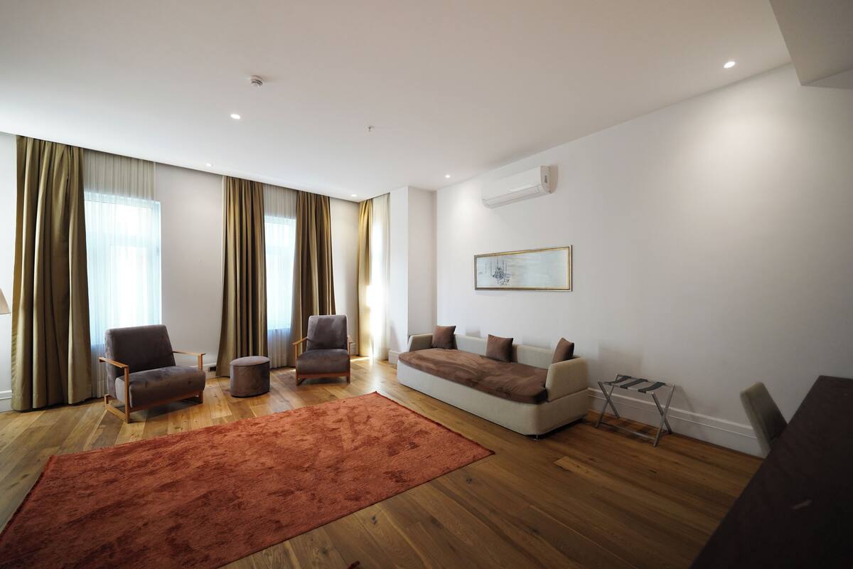A modern living room with a sofa, armchairs, a coffee table, and a large window with curtains.