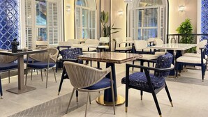 Un área de estar interior moderna con mesas y sillas, ventanas amplias con contraventanas e iluminación decorativa.