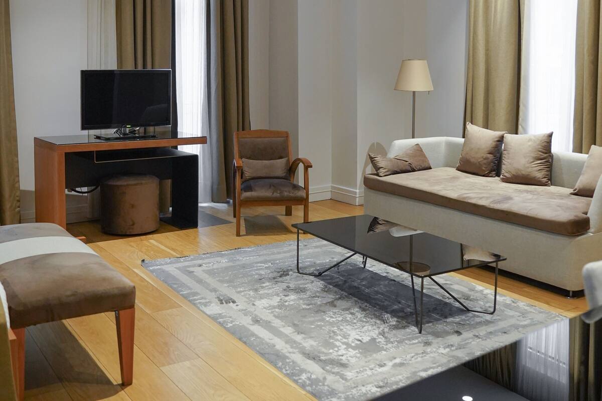 A modern hotel room with a sofa, a chair, a TV, a lamp, and a coffee table.