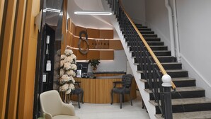 Zona de recepción de un hotel con escalera, mostrador de recepción y área de descanso.