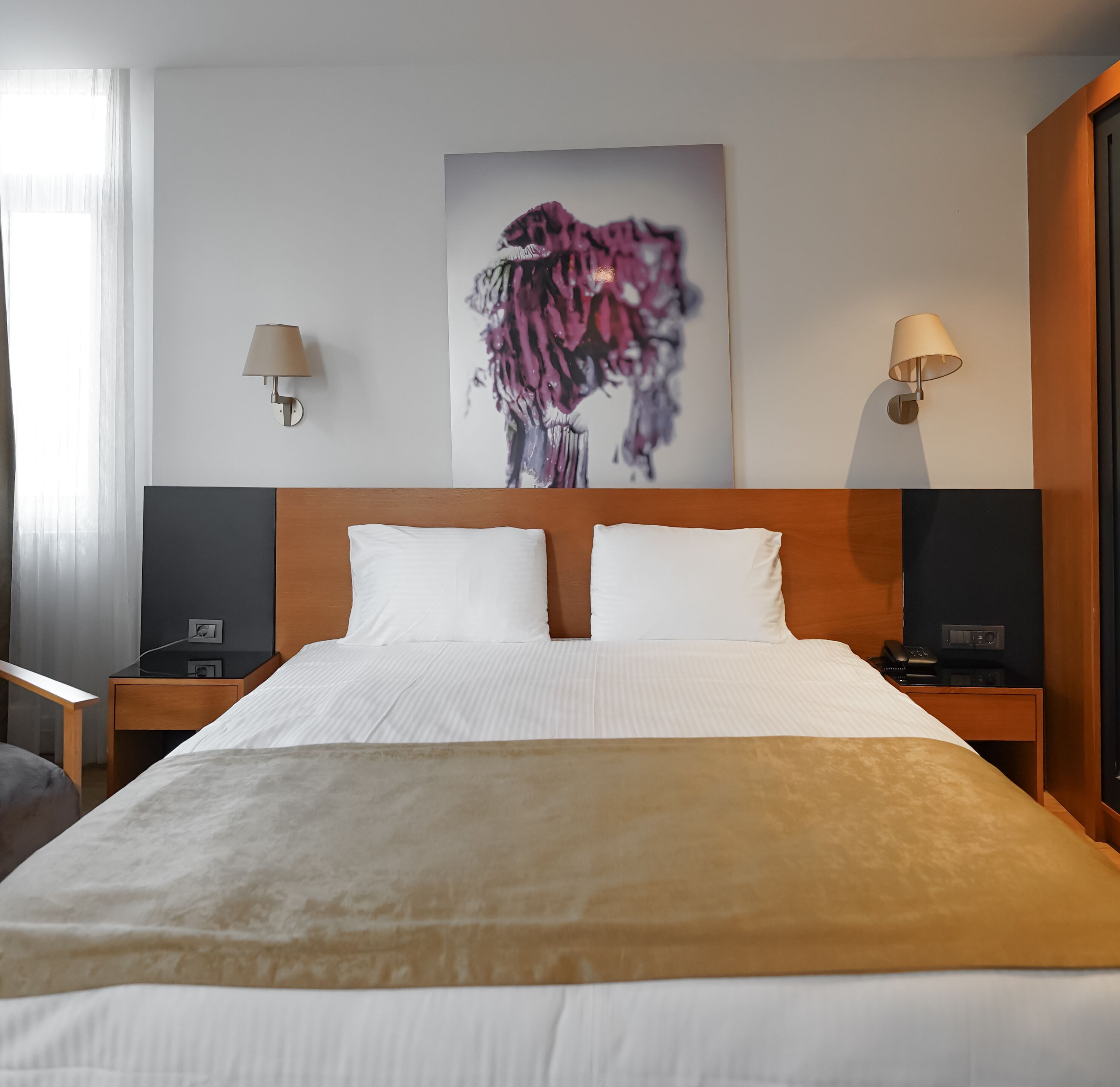 Une chambre d’hôtel avec un grand lit, deux tables de chevet, une lampe fixée au mur et un tableau.