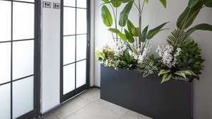Un pasillo con un ventanal grande, una puerta con el símbolo de baño, y una jardinera con diversas plantas y flores.