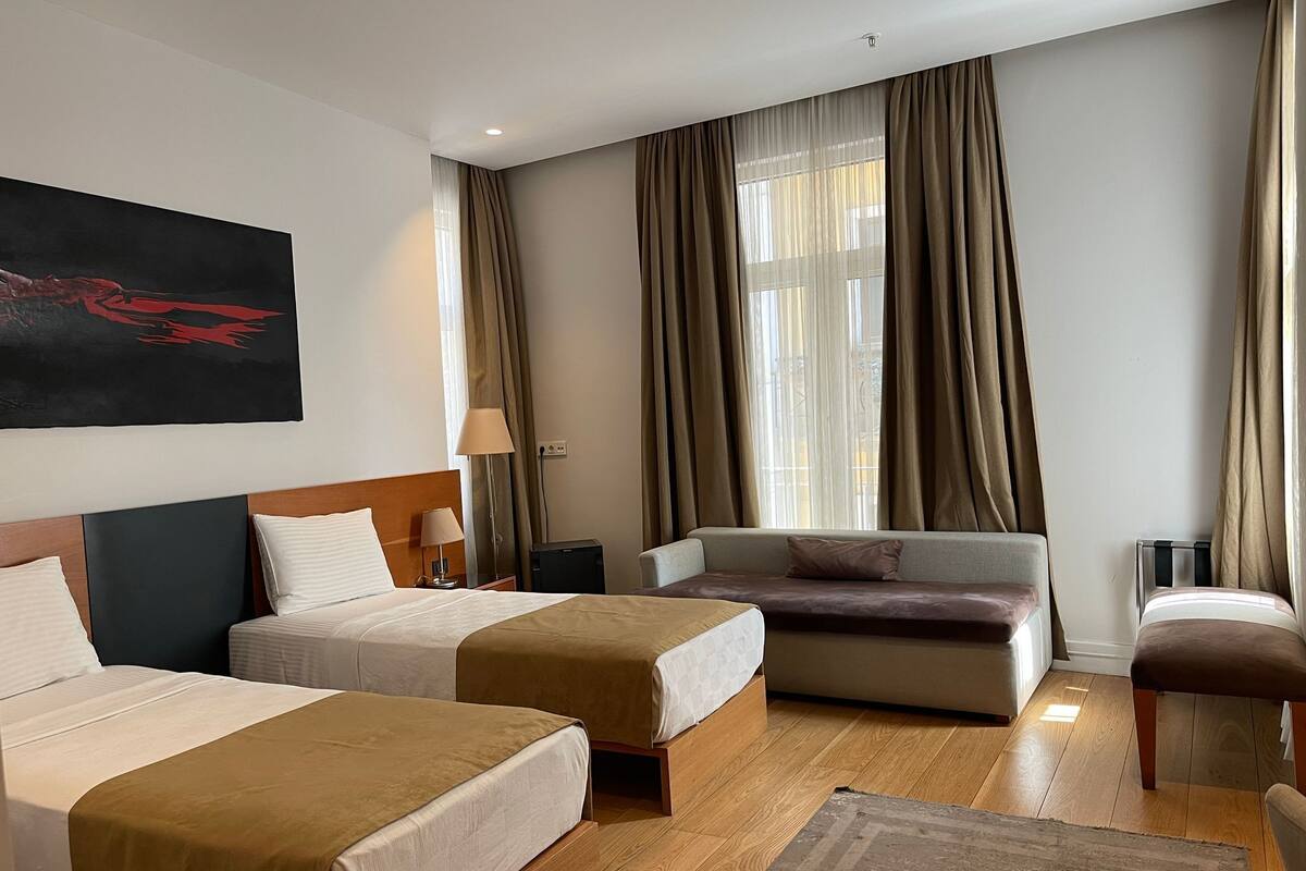 A hotel room with two beds, a sofa, a chair, and a large window with curtains.