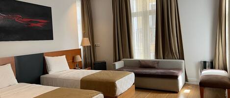 A hotel room with two beds, a sofa, a chair, and a large window with curtains.
