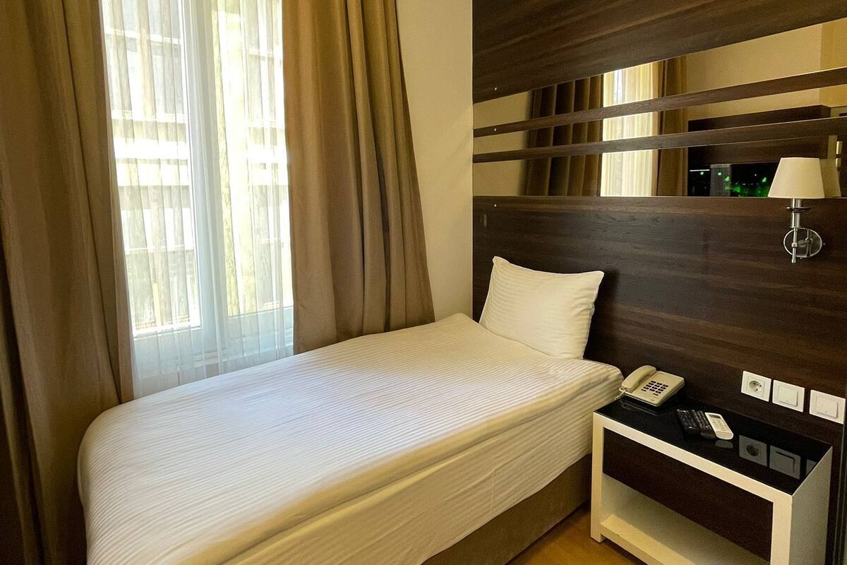 A hotel room with a single bed, a bedside table with a lamp, a phone, and a power outlet.