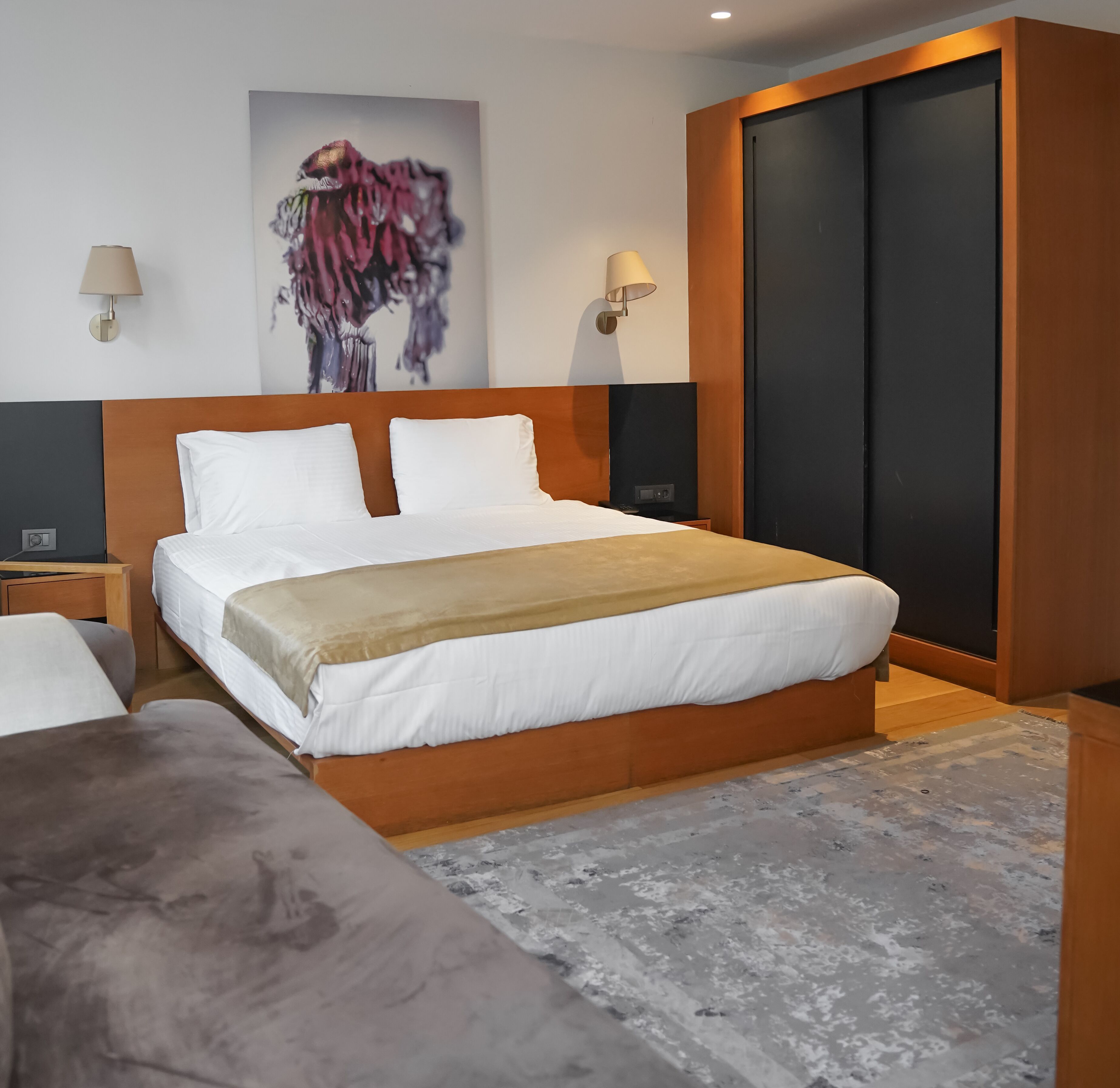 Habitación de hotel moderna con una cama grande, cabecera de madera, un cuadro en la pared y un armario.