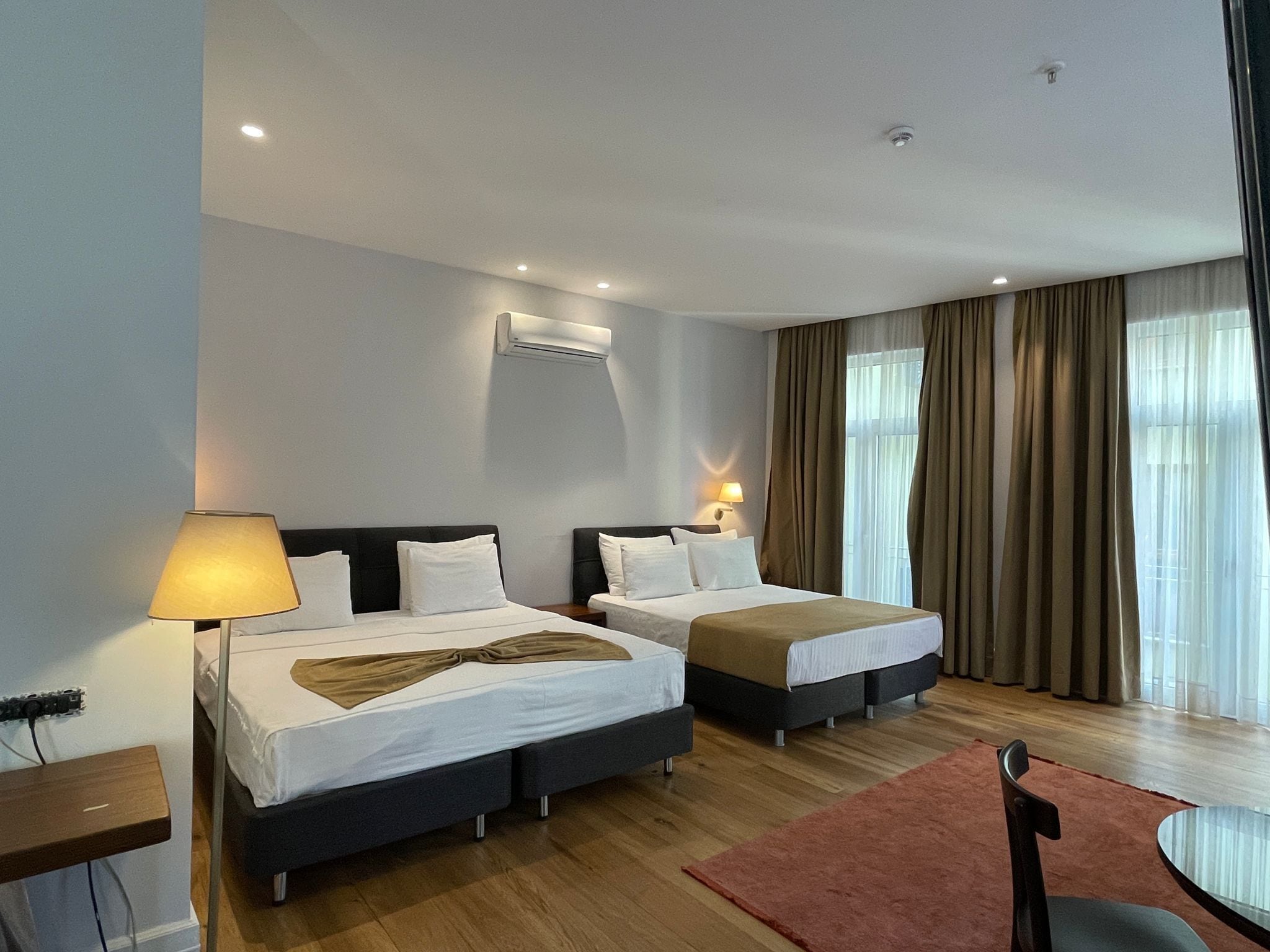 A hotel room with two beds, a desk, a chair, and a dining table.