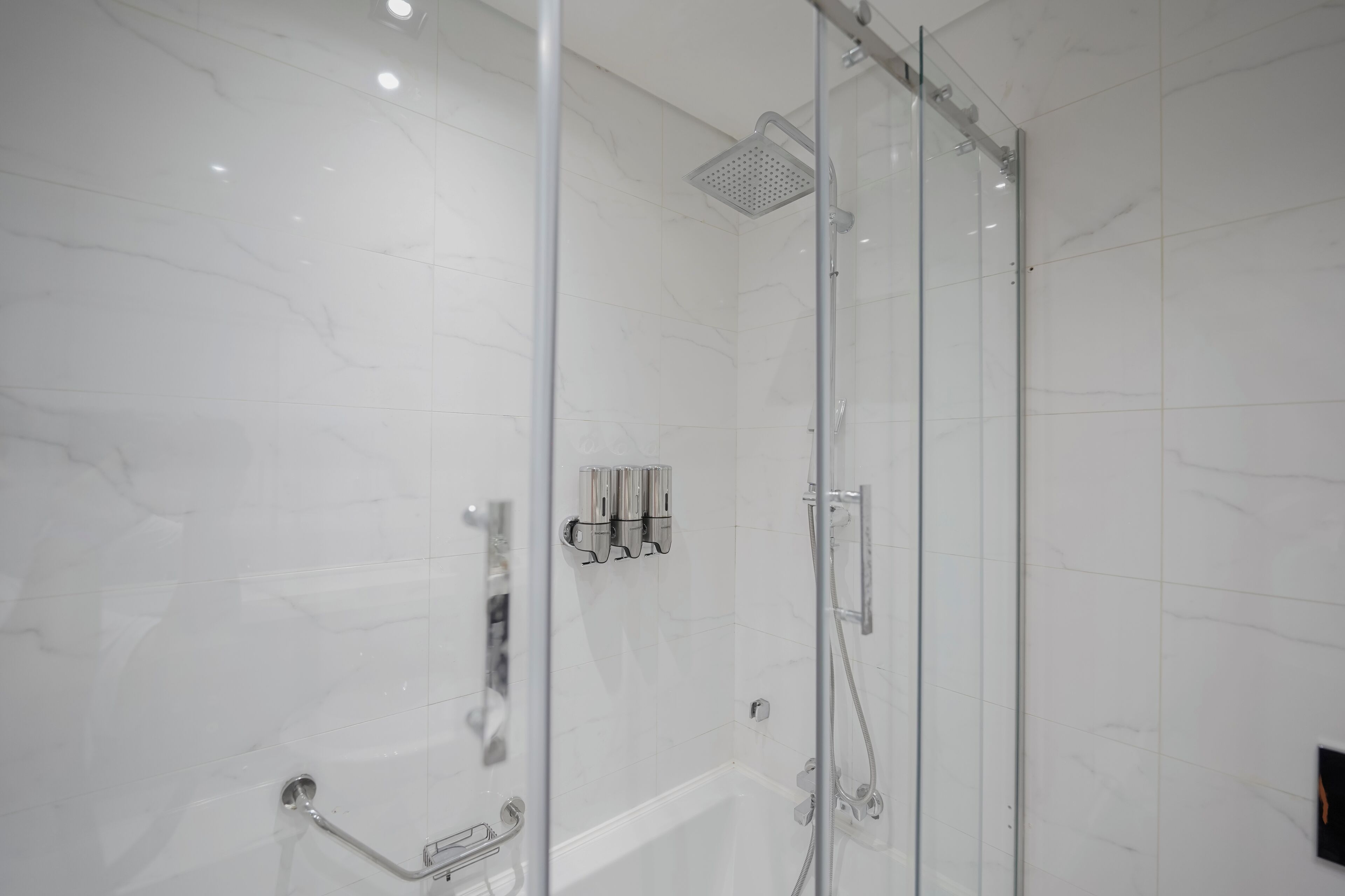 A modern bathroom with a glass-enclosed shower, a white marble wall, and a handrail.