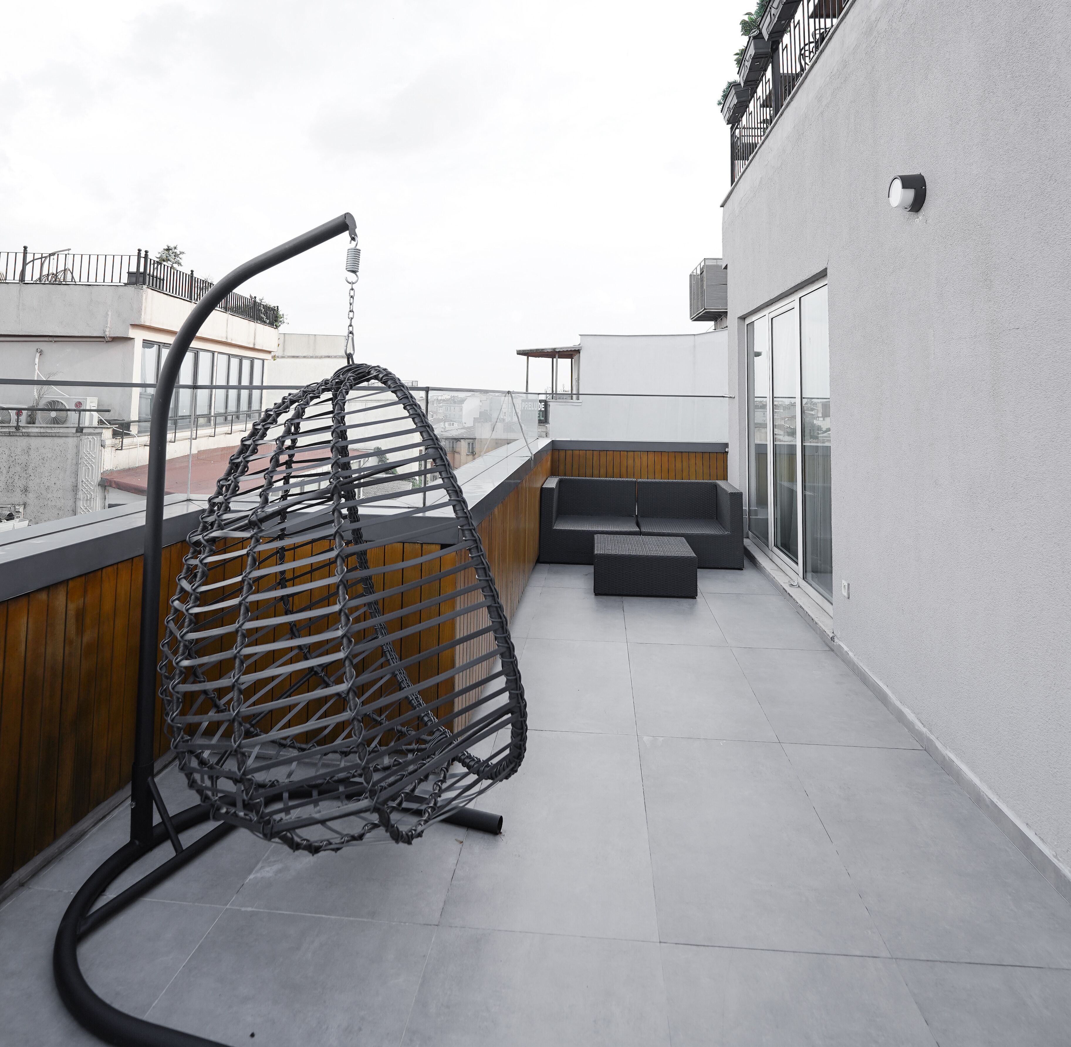 A rooftop terrace with a hanging chair, a cushioned bench, and a glass balustrade.