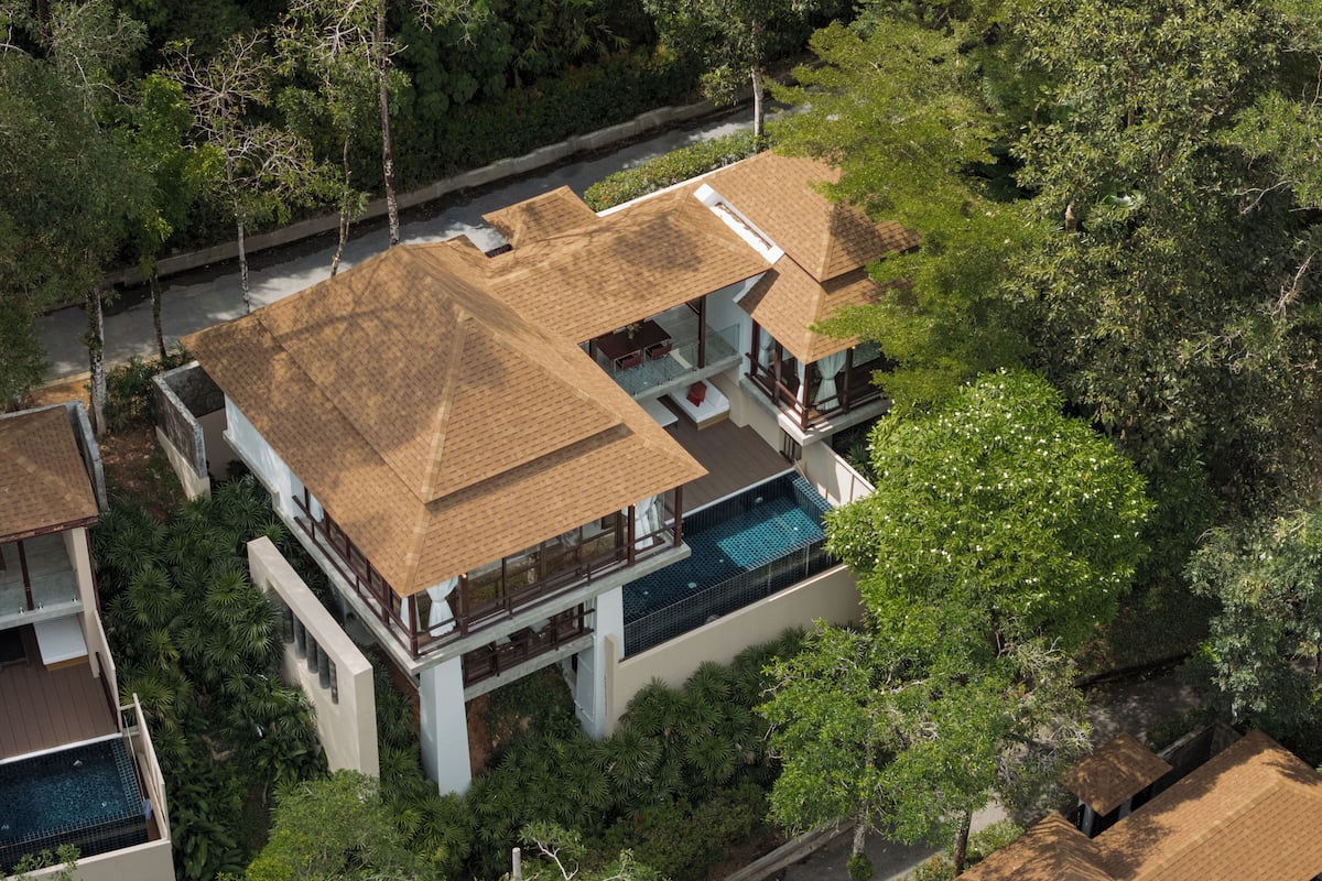 Una casa moderna de varios pisos con una amplia terraza en la azotea, piscina y abundante vegetación alrededor.