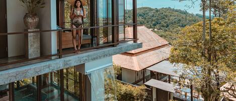 A modern house with a large balcony overlooking a swimming pool and lush greenery.
