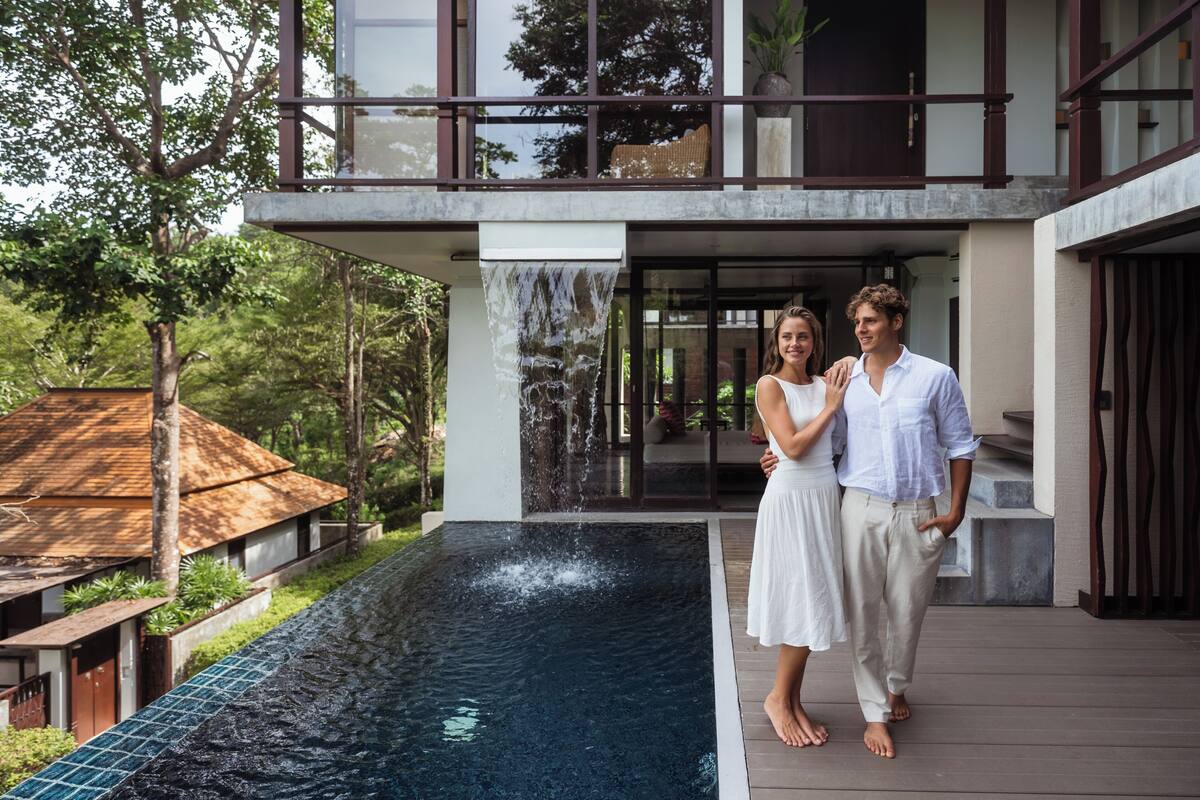 Una casa moderna con una gran piscina exterior, una terraza de madera y un balcón de dos pisos.