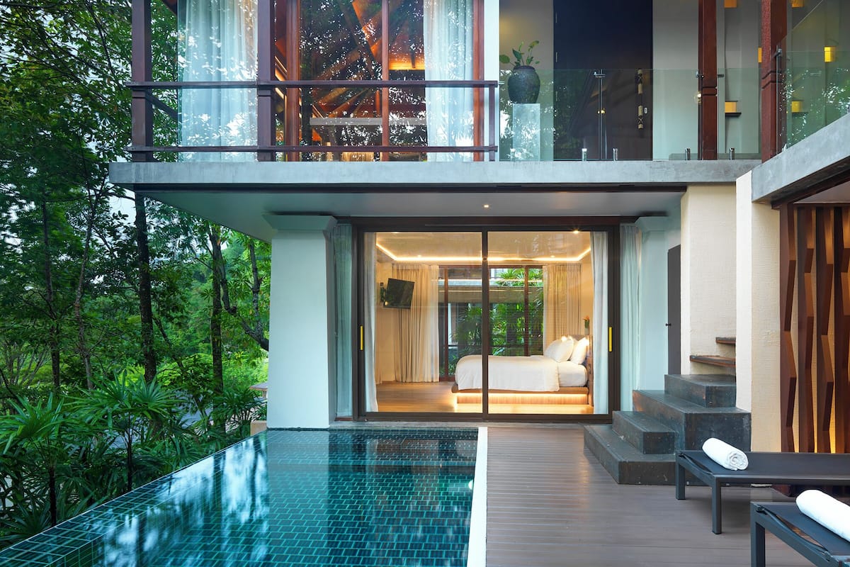 Una casa moderna con puerta de cristal que da a un dormitorio, piscina y balcón con vistas a la vegetación.