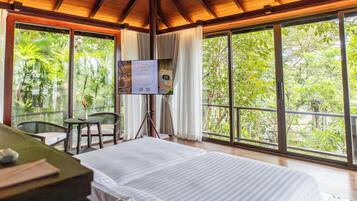 A room with a bed, a table, a chair, and a TV screen displaying a Thai cooking class.