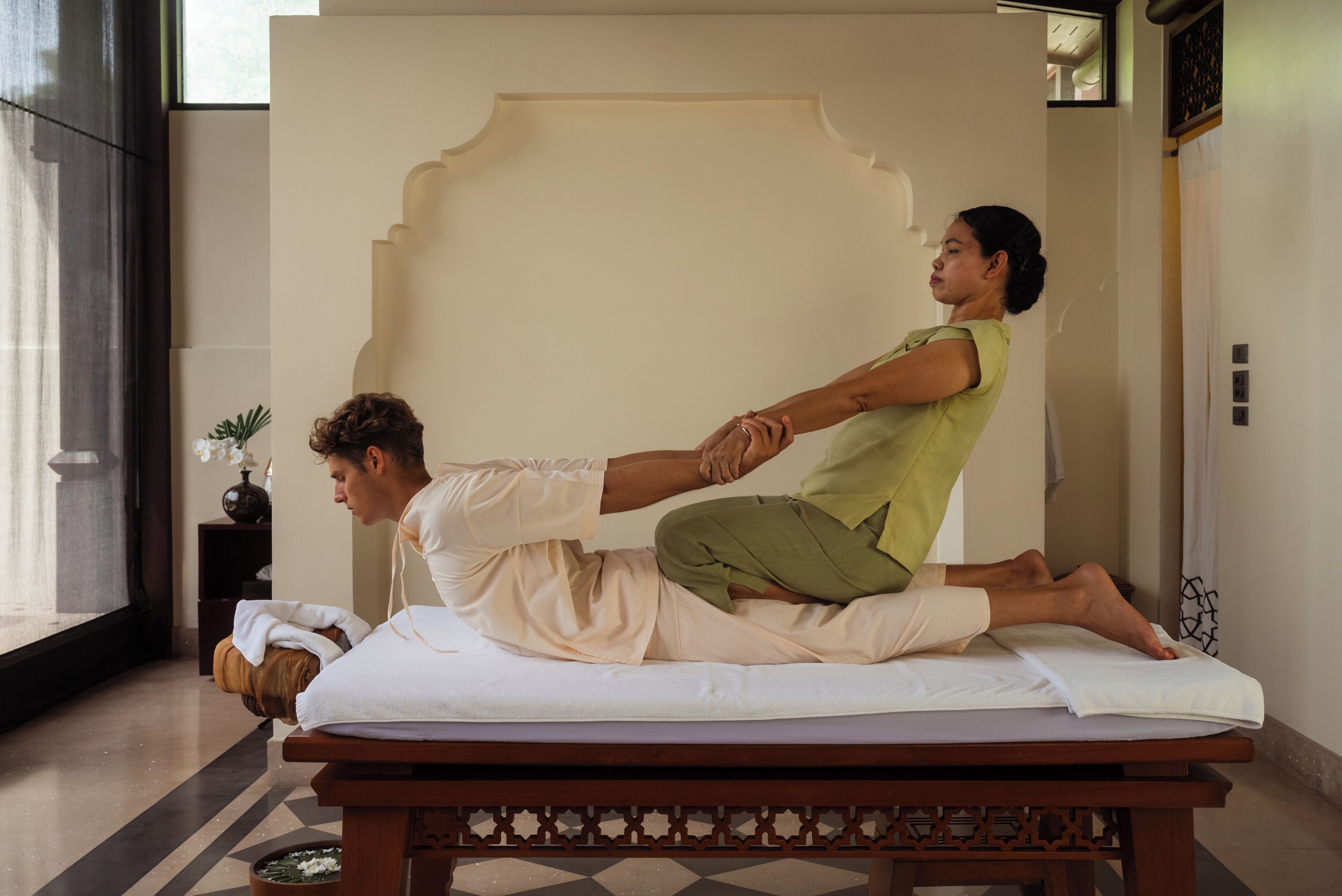 A massage therapy session in a room with a large window, a decorative wall, and a wooden massage table.