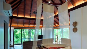 Un baño moderno con una bañera independiente, un banco de madera y un amplio ventanal con vistas al exterior.