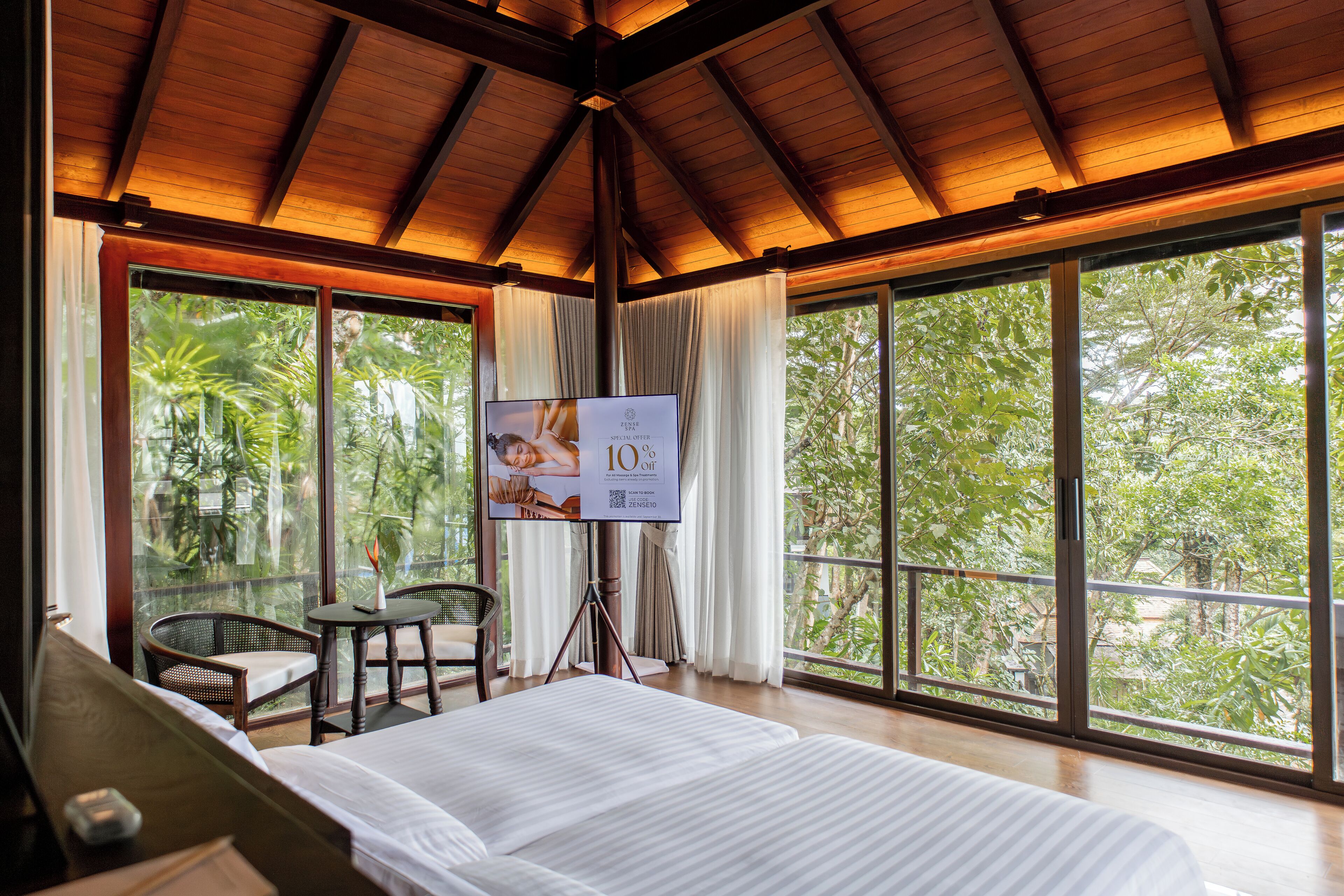 A hotel room with a large bed, a small table, a chair, and a TV screen displaying a spa advertisement.