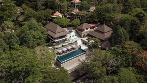 Vista aérea de un complejo turístico con varias edificaciones rodeadas de bosque denso, una piscina y una escalera que conduce a una zona en la azotea.