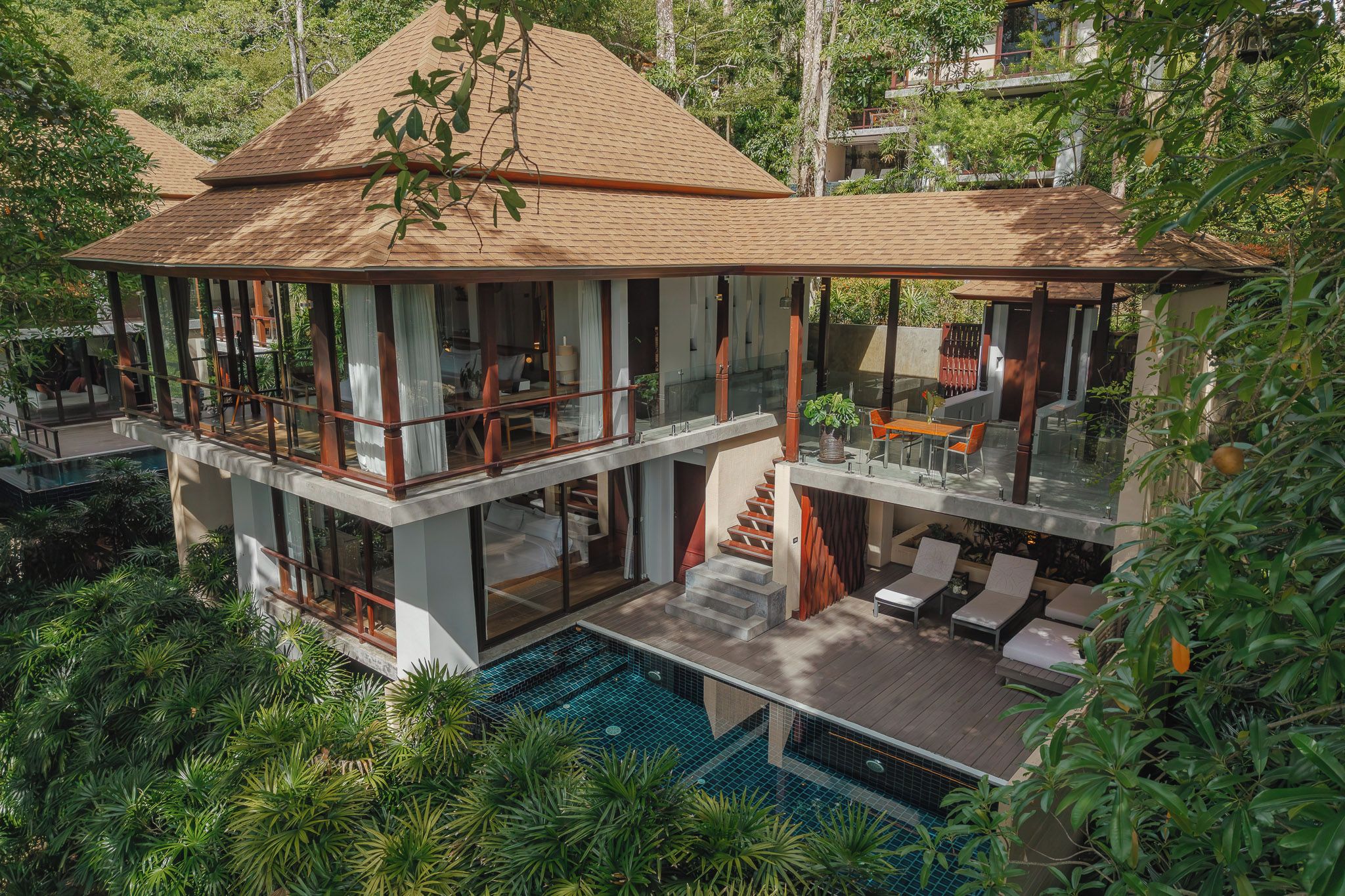Una casa de varios niveles con piscina, zona de estar exterior y abundante vegetación.