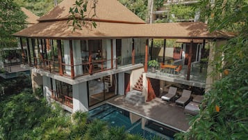 Una casa de varios niveles con piscina, zona de estar exterior y abundante vegetación.