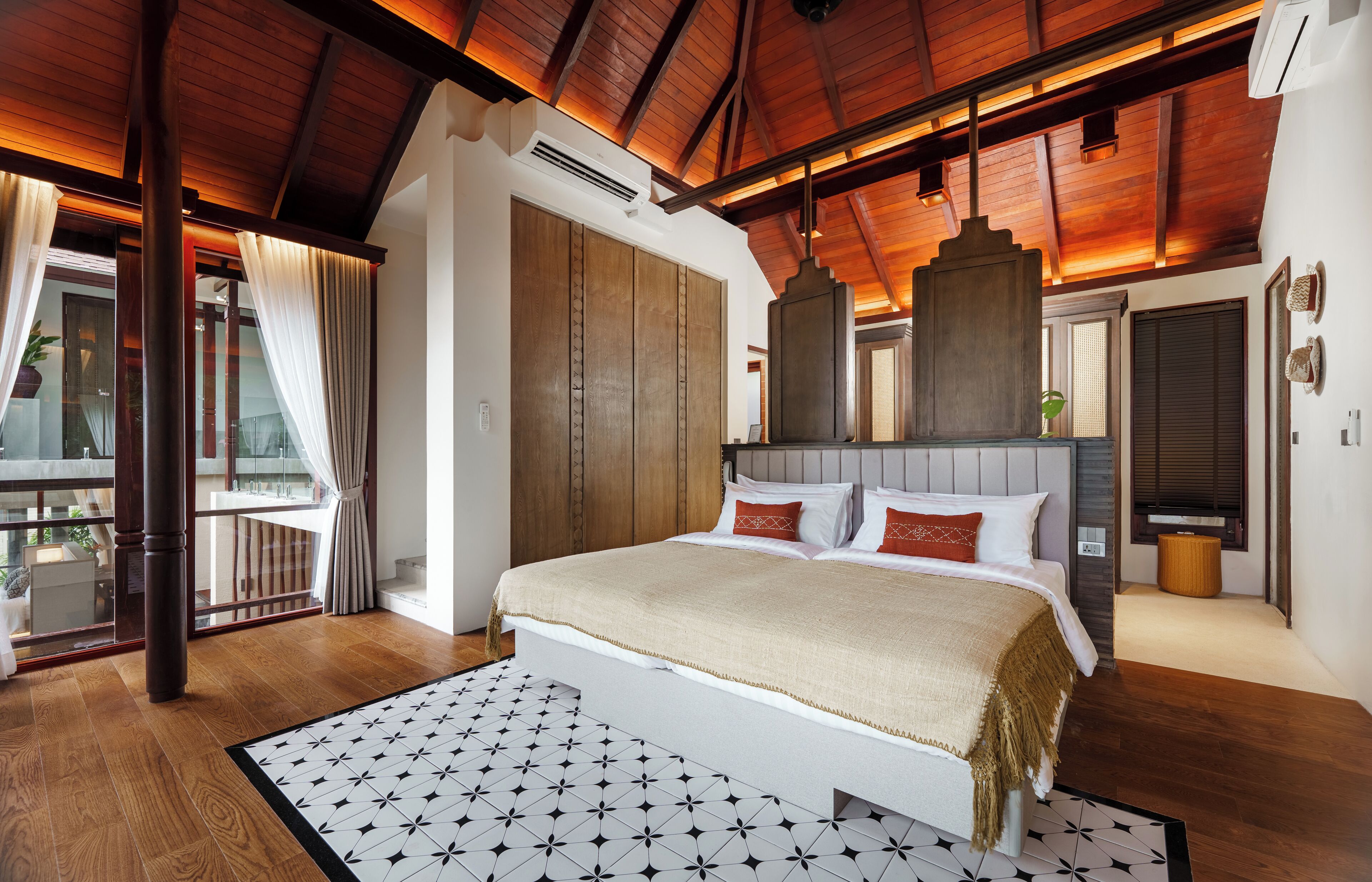 A bedroom with a large bed, wooden ceiling beams, and a view of the outdoors.