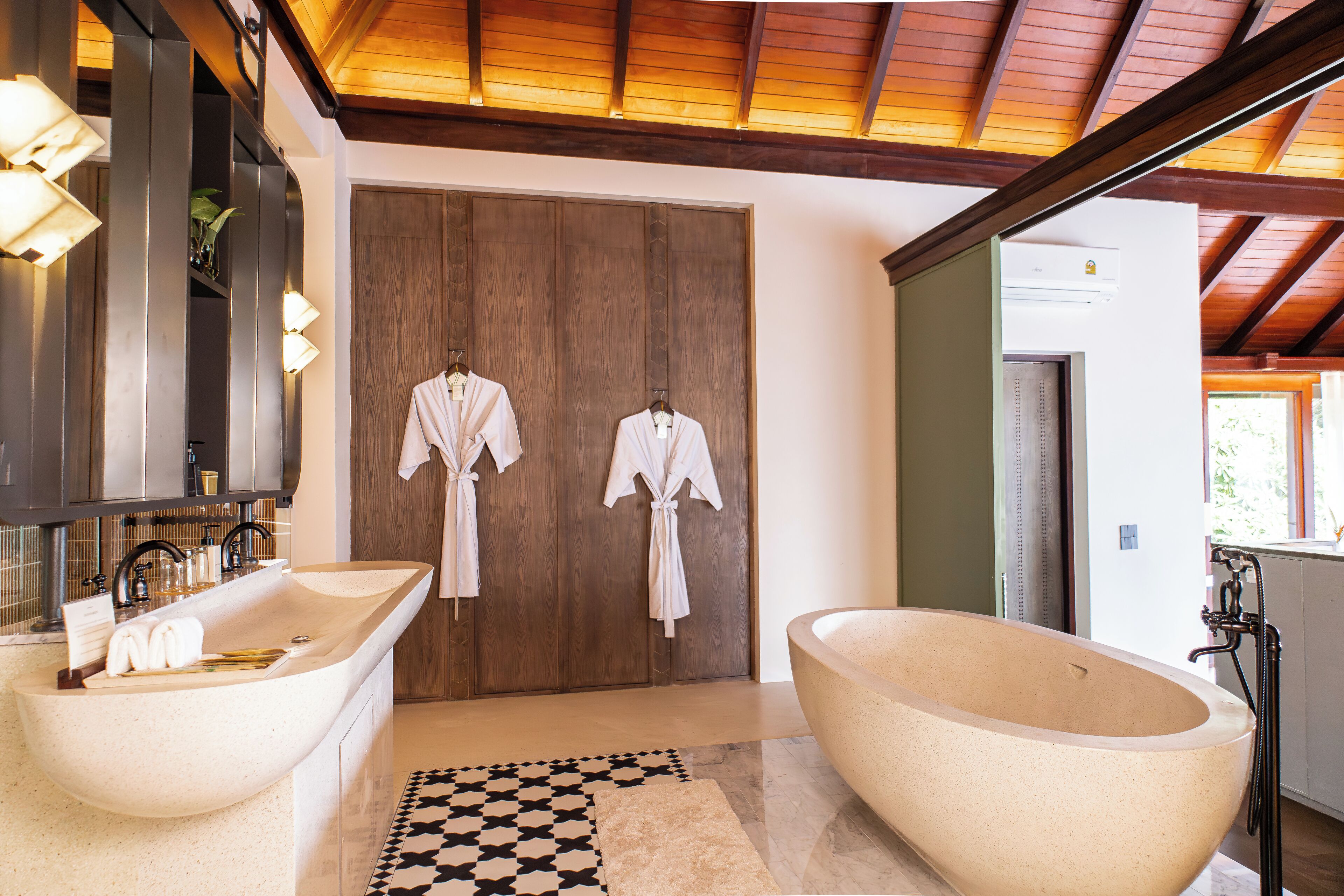 A modern bathroom with two large freestanding tubs, a wooden door, and a checkered rug.