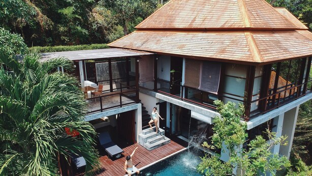 Una casa moderna de dos pisos con piscina, mobiliario exterior y vistas al bosque circundante.